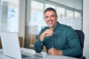 A man in a green shirt sitting at a desk with a laptop